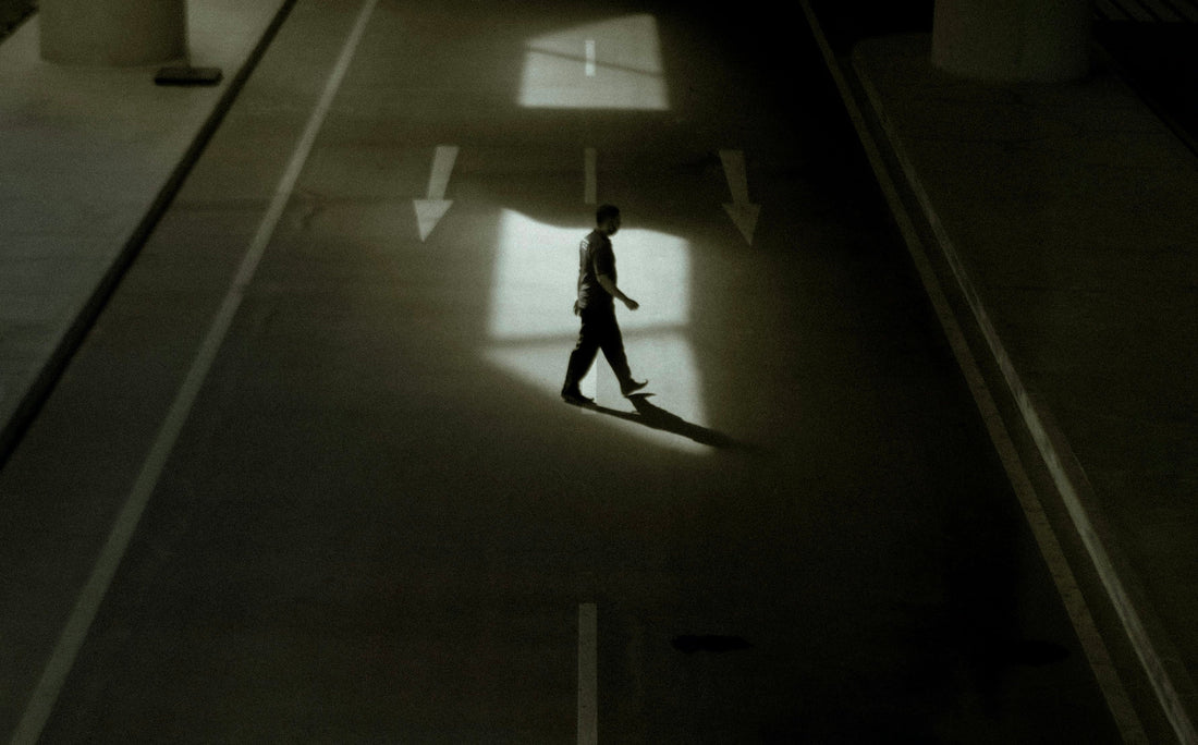 A single peson crossing the road in the light surrounded by a shadow