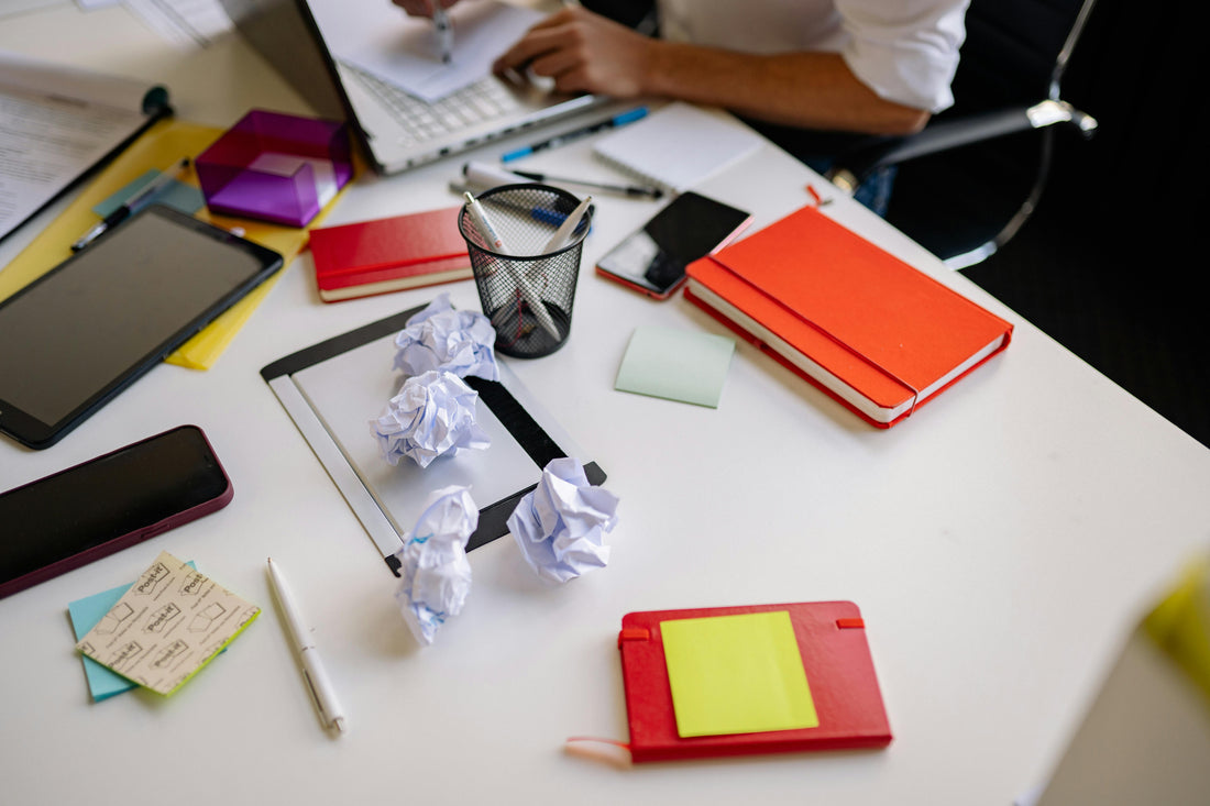 Unorganized desk with scattered papers, pens and notebooks