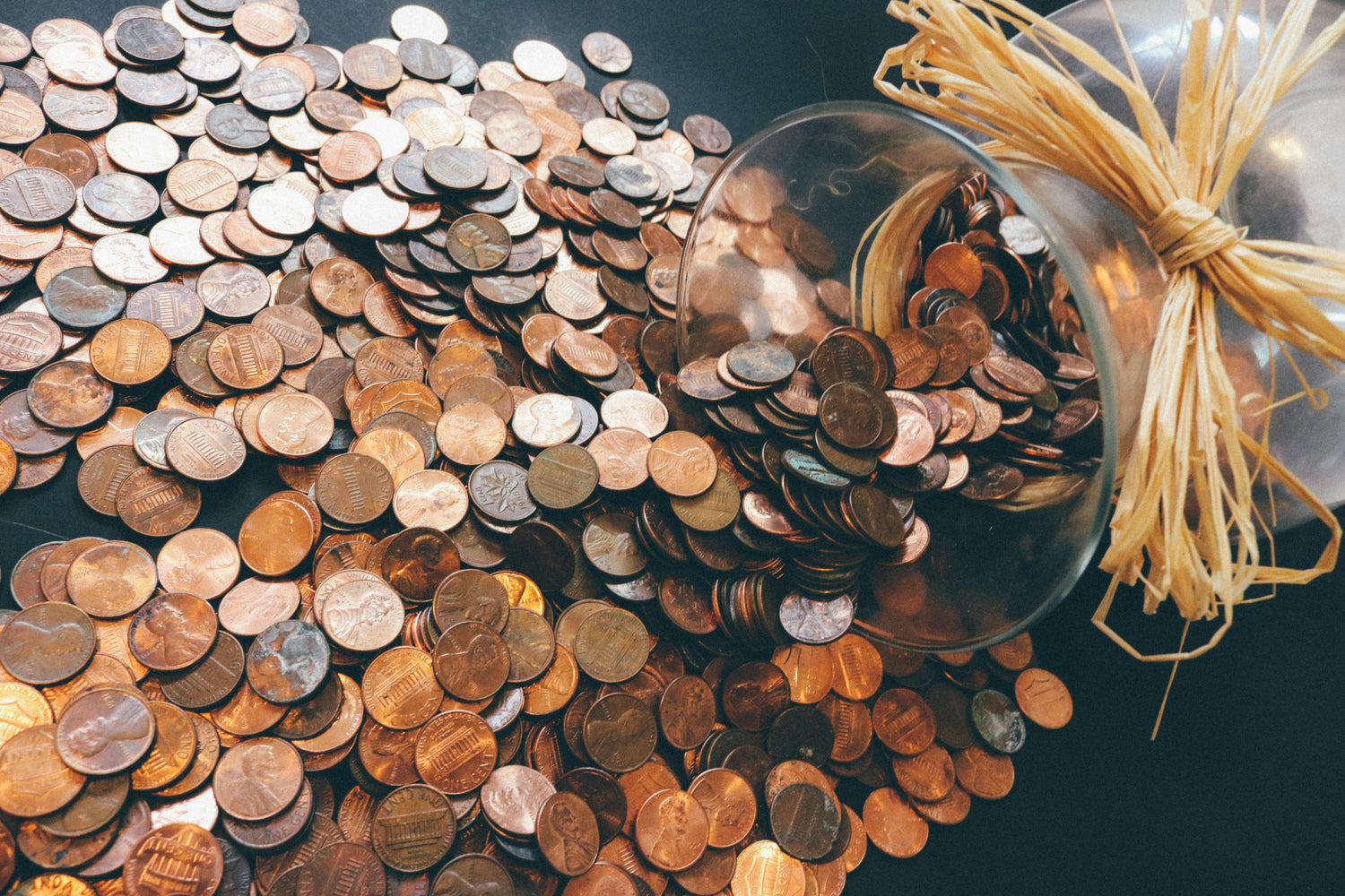 Pile of coins with a glass bowl and straw on a dark surface