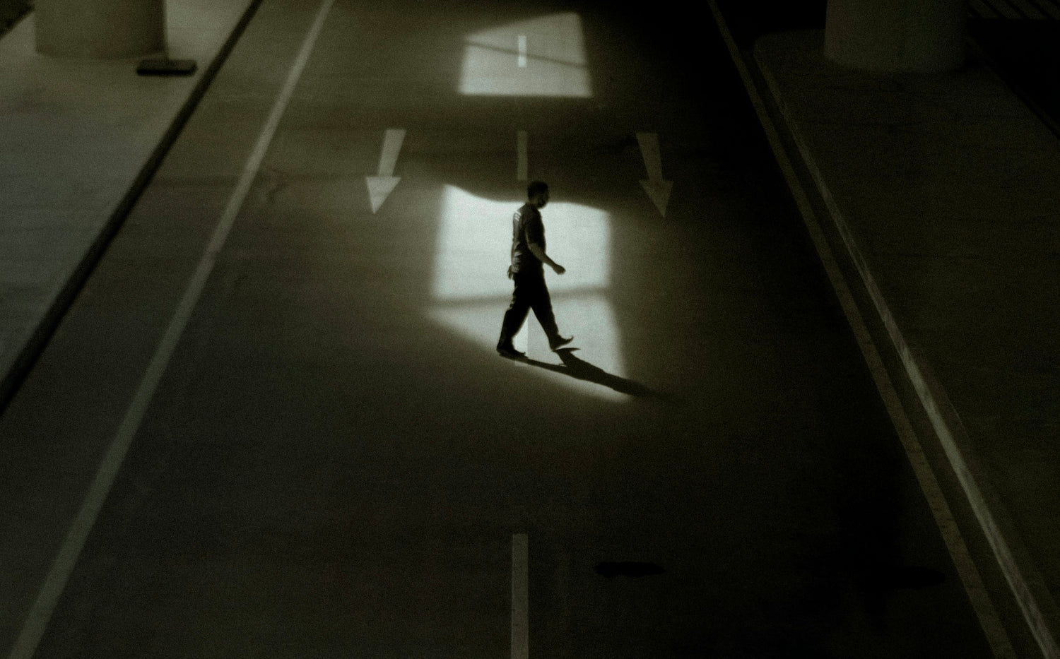 Person crossing the middle of the road with no one else around in a dark atmosphere.