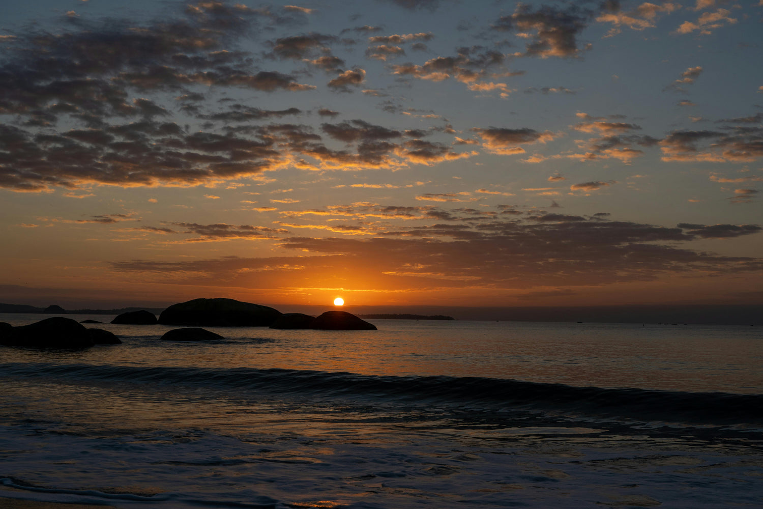 Sunset over the ocean with rocks and clouds