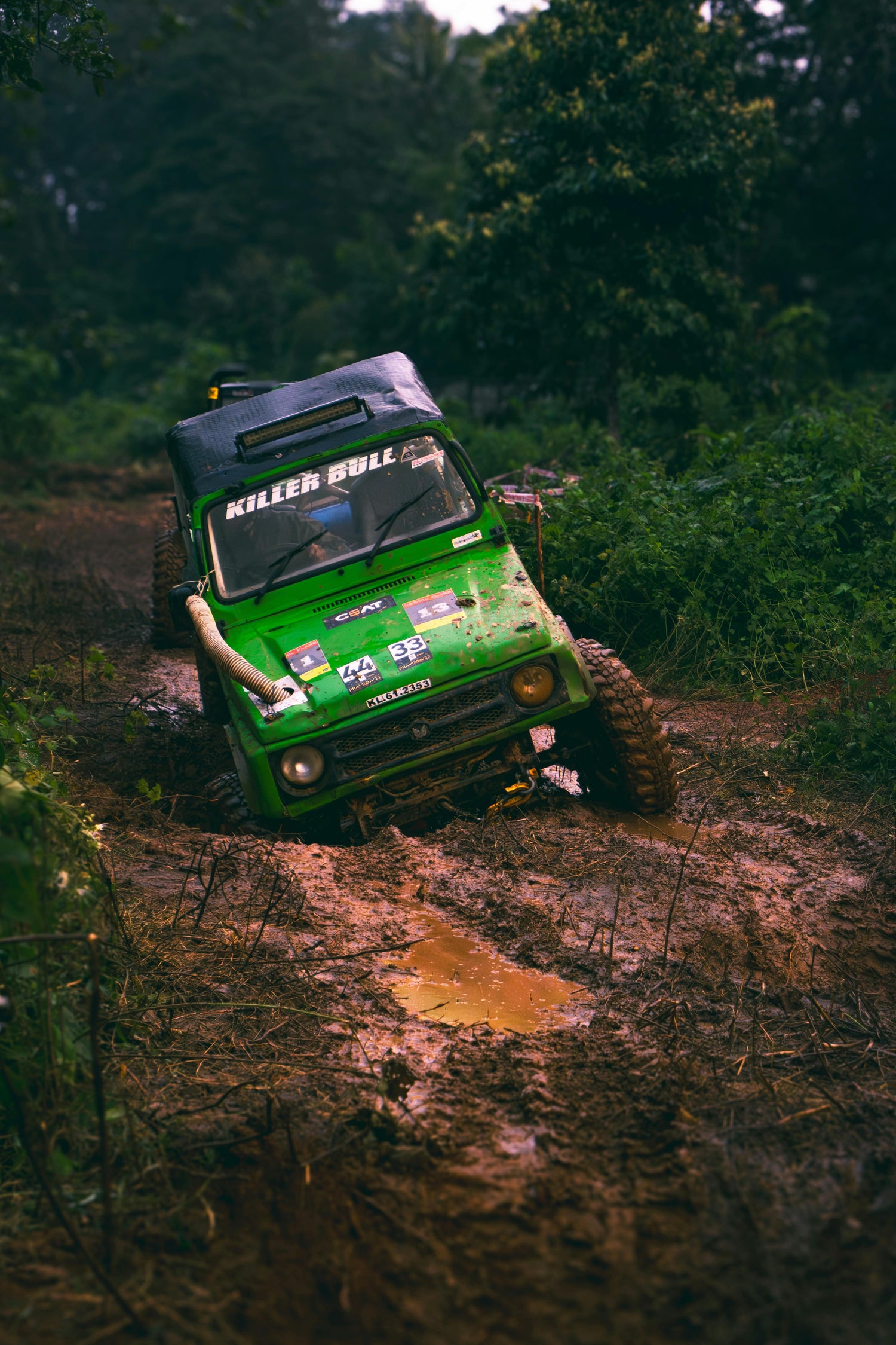 Green off-road vehicle navigating a muddy path in a forest