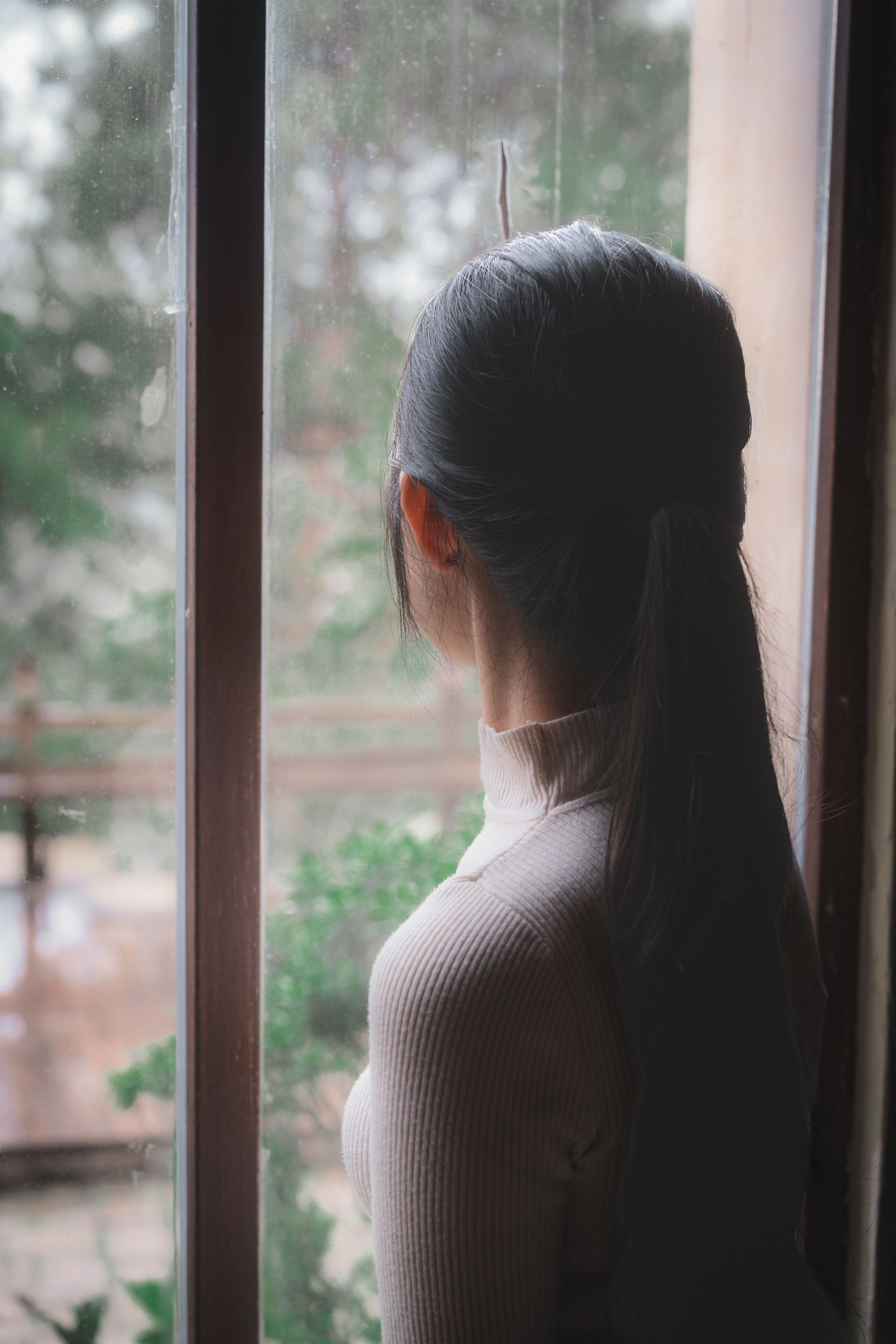 A serene woman with long hair looks out a window, contemplating nature and decluttering her mind.